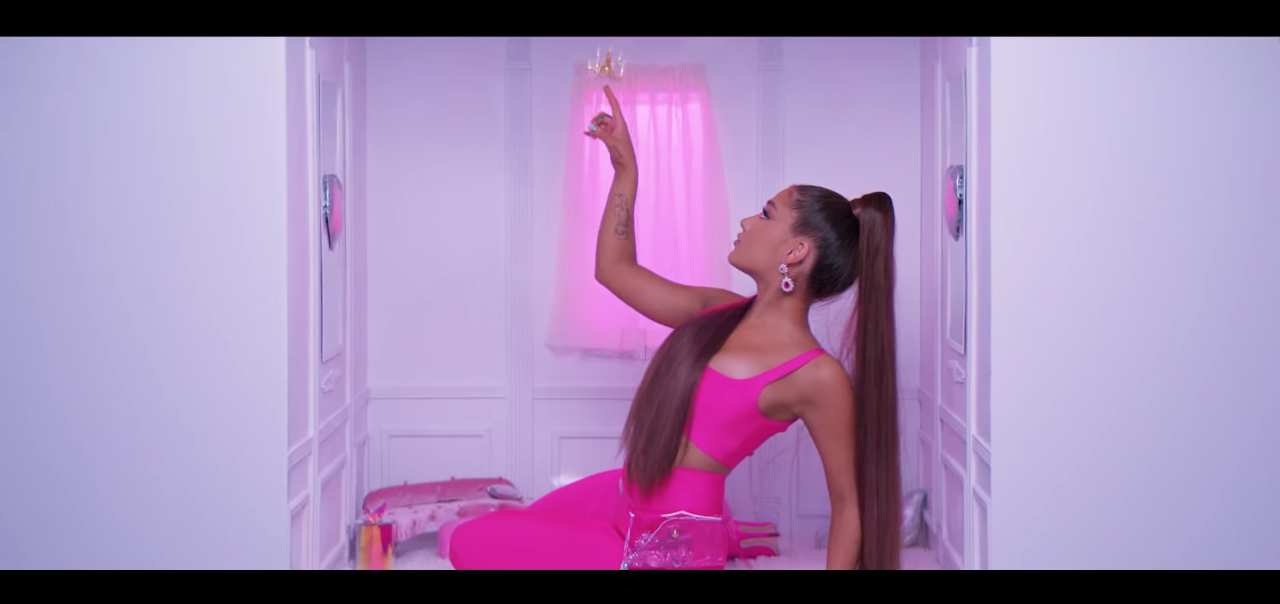Ariana Grande is dressed in hot pink—tight cropped vest and high waisted tr...
