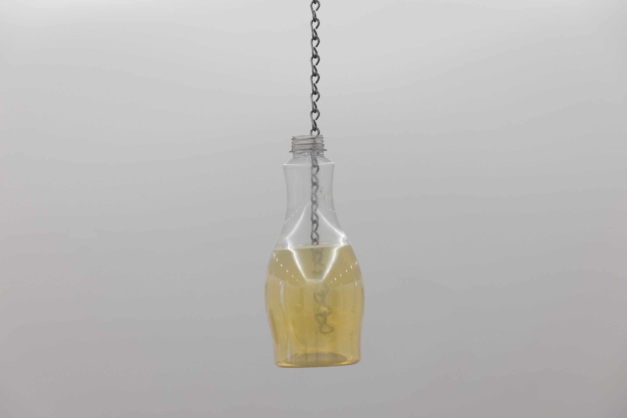 a plastic bottle filled with a yellow liquid, hanging from the ceiling by a chain submerged in the liquid.
